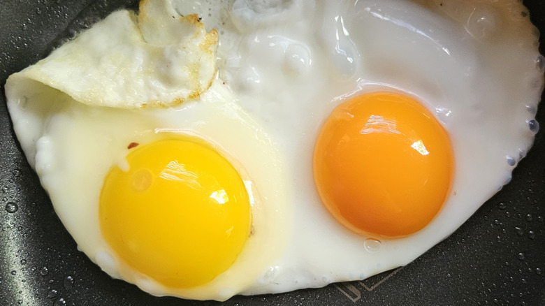 Two eggs with orange and yellow yolks being fried in a pan