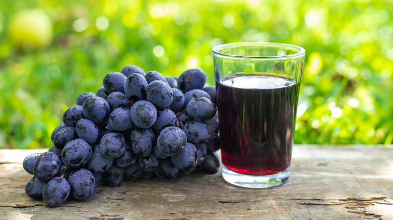 bunch of red grapes with a glass of red grape juice beside them