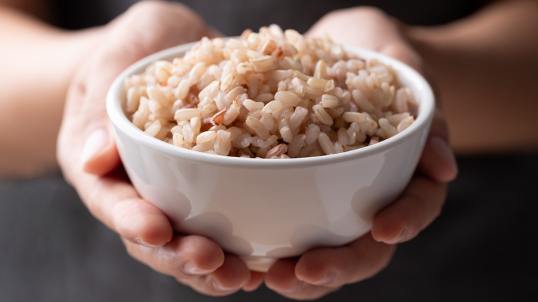 Hands holding white bowl of cooked brown rice