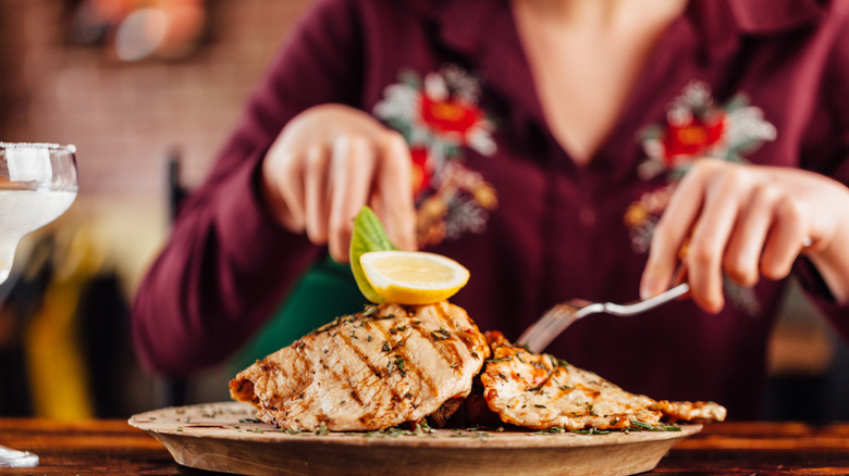 Person cutting cooked chicken breast on a plate