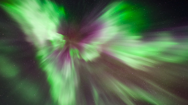 Streaks of green and purple light converge on a single point overhead in the night sky