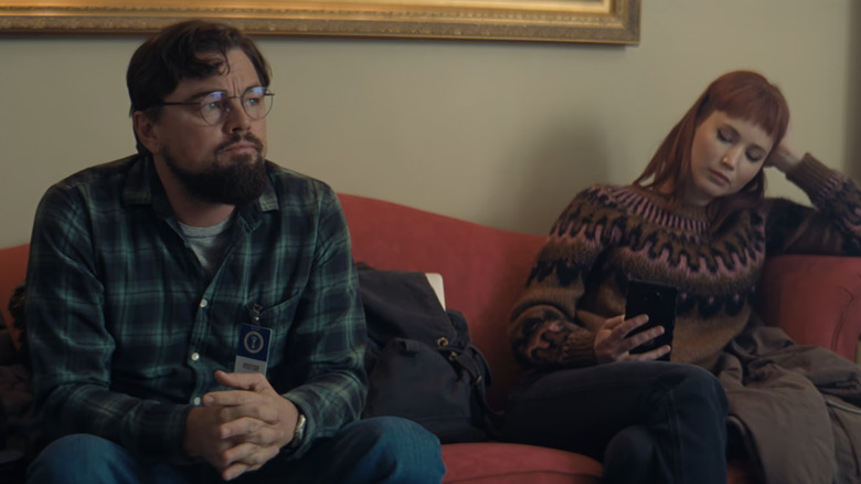 Leonardo DiCaprio's Dr Randall Mindy sits next to Jennifer Lawrence's Kate Dibiasky on a red couch in Don't Look Up