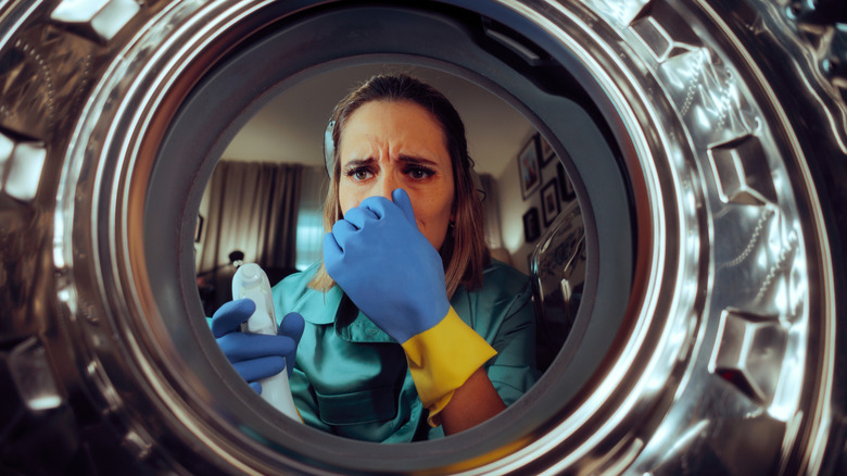 Woman with rubber gloves pinches her nose while pointing cleaning spray bottle