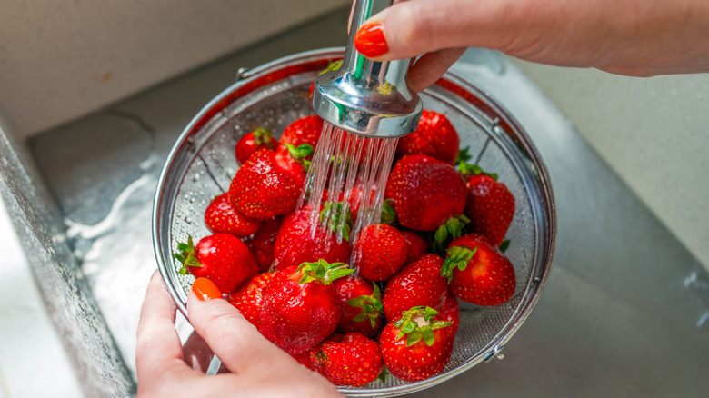 Strawberry being washed under the faucet