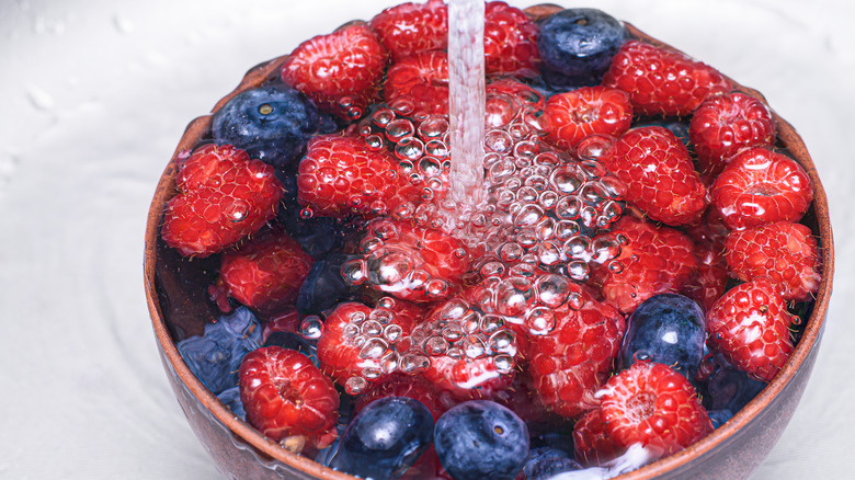 Blueberries and raspberries in a bowl of water, with water being poured on top