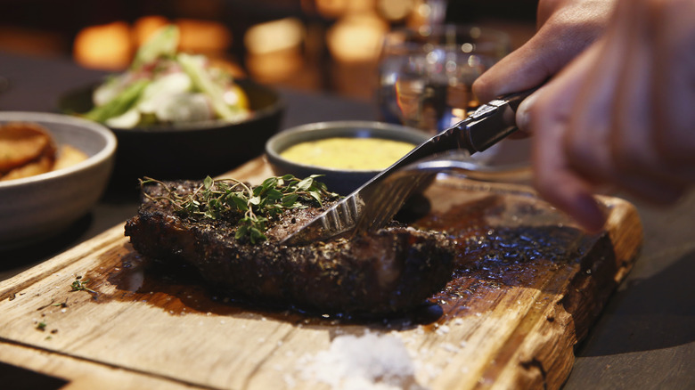 Hands cutting a steak on a board