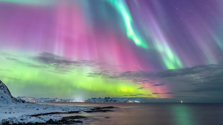 An aurora is seen in the night sky above a city in a snowy landscape