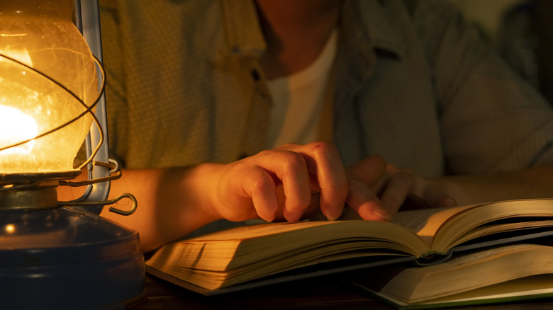 Person reading a book by lantern light
