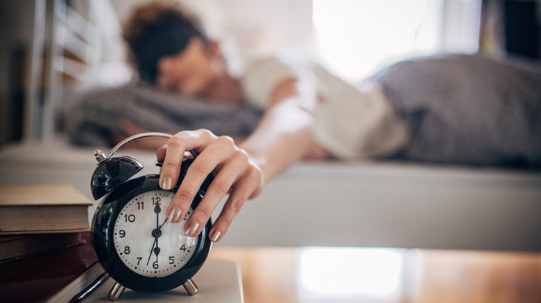 Woman waking up and turning off an alarm clock