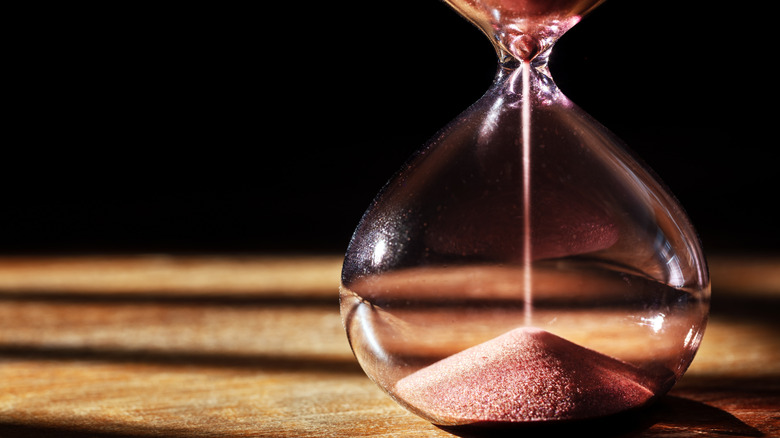 Hourglass emptying in a shaft of light in an otherwise dark room.