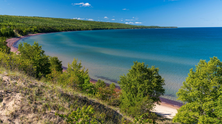 A cobalt blue lake and sandy shore with green trees lining it