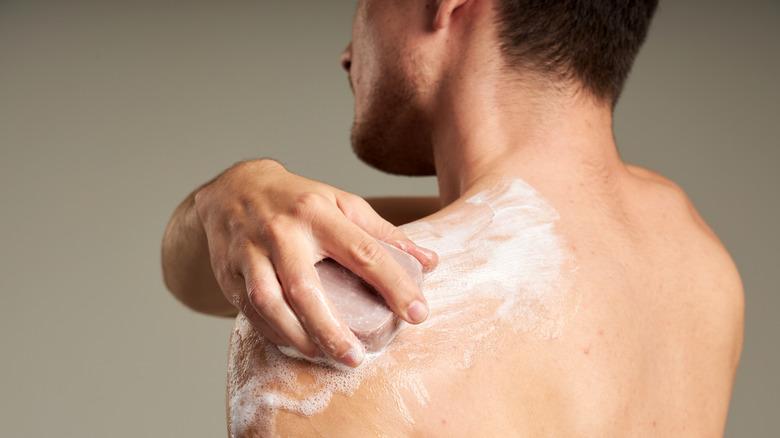 Man washing his back in the shower, using his hand to move the bar of soap