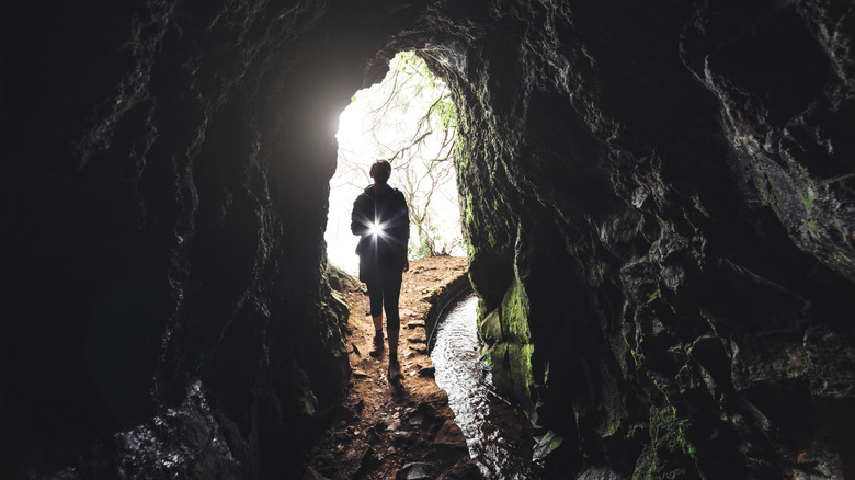 silhouette of person entering dark cave with flashlight