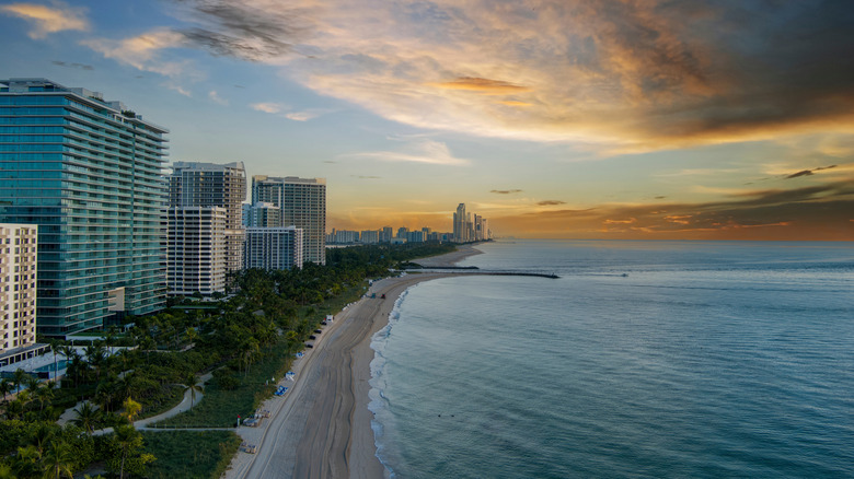A shot of the Miami coastline shows the ocean and skyscrapers below a sunset