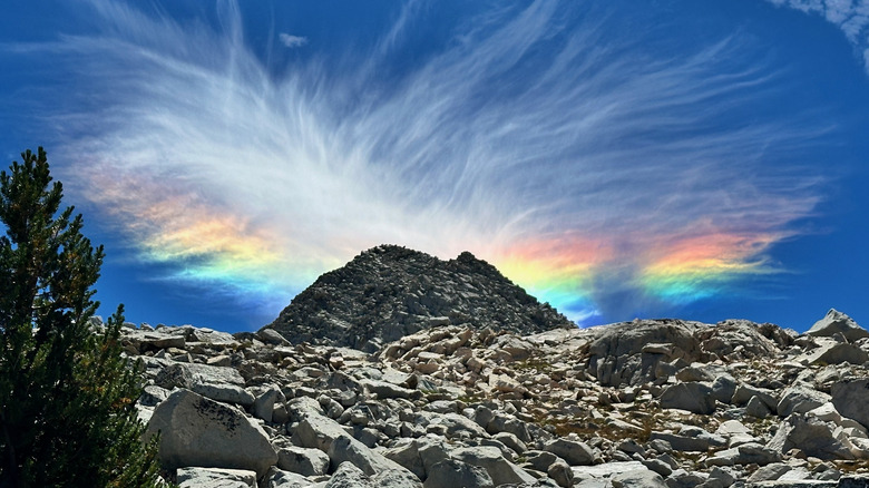 A rock outcropping with a fire rainbow in the sky behind it, thin wispy clouds