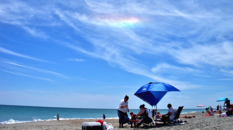 People on a beach with a rainbow-colored fire rainbow in the sky