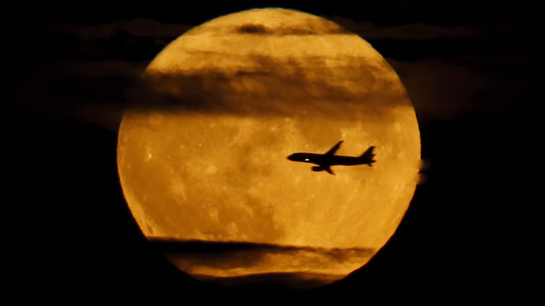 Plane flying and light clouds streaking in front of an orange-yellow Sturgeon Moon