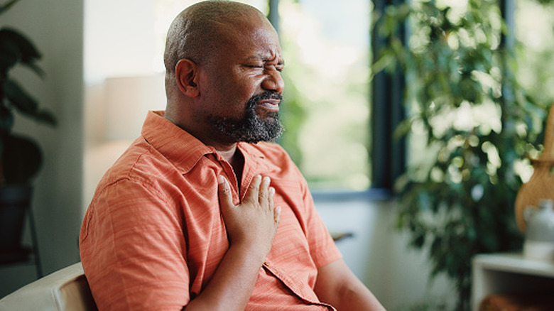 Man sitting on sofa with hand on middle of chest in discomfort