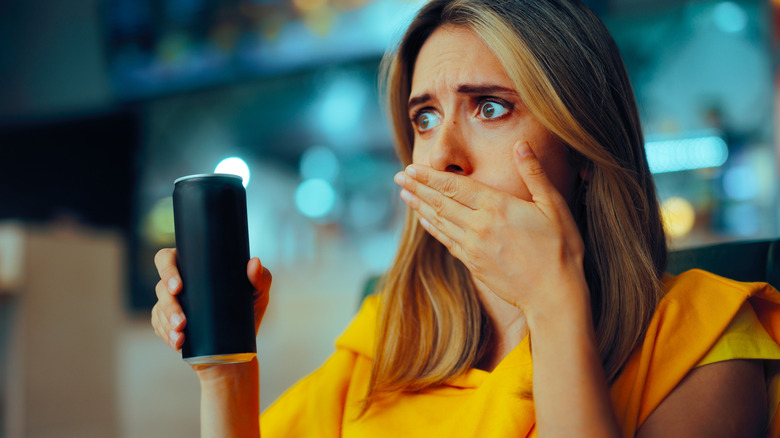 Woman covering mouth while holding a canned beverage in hand
