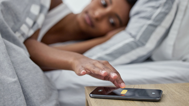 A young woman reaching for her phone to turn off an alarm.