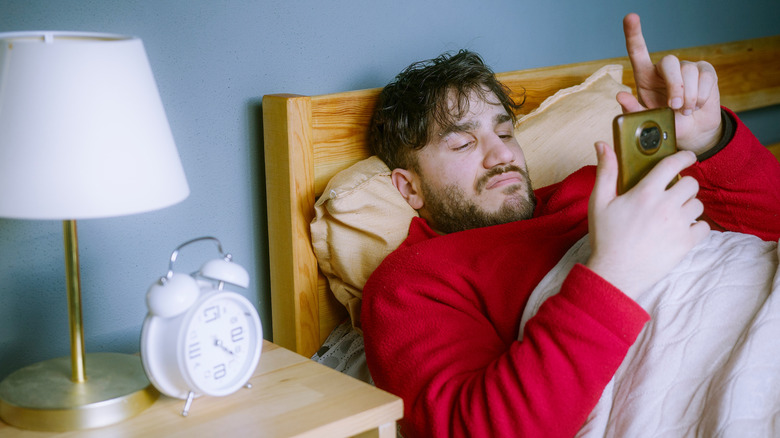 A man laying in bed while scrolling on his phone.