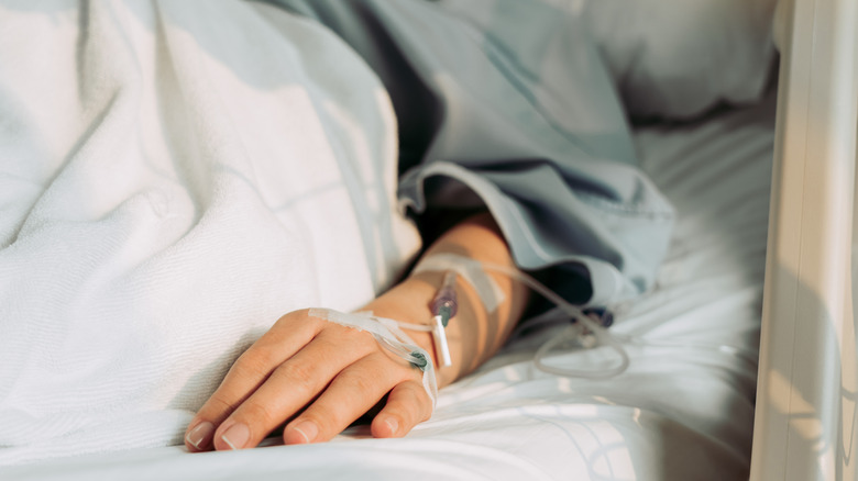 Arm and hand of a woman lying in hospital bed with IV tube connected to her hand