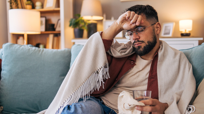 Man sitting on sofa with blanket and hand on forehead