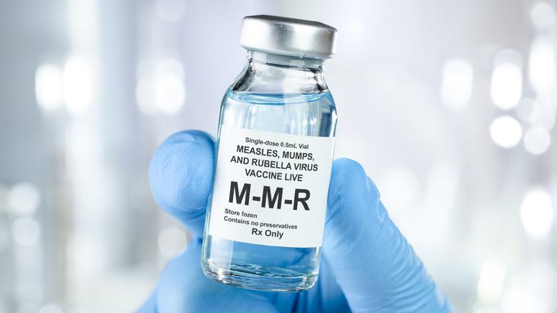 A gloved hand holding an MMR vaccine vial