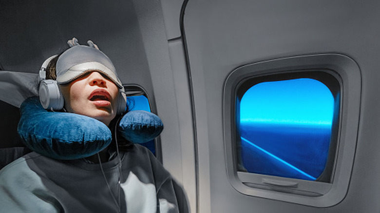 Woman in window seat of plane with eye mask and neck pillow