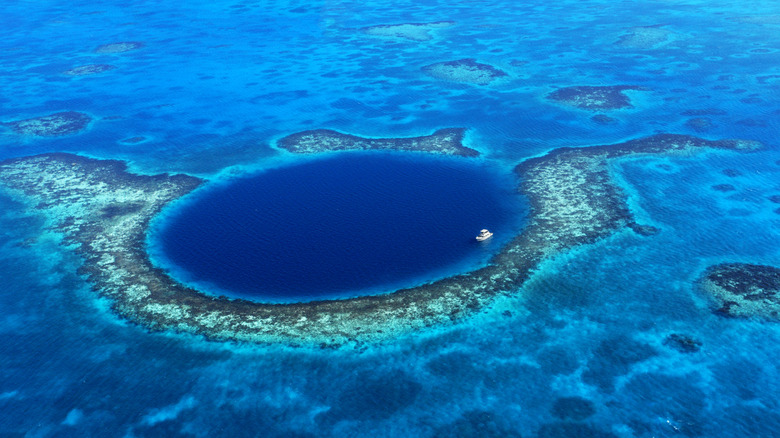 The Great Blue Hole off coast of Belize, large dark blue circle in ocean with tiny boat for scale