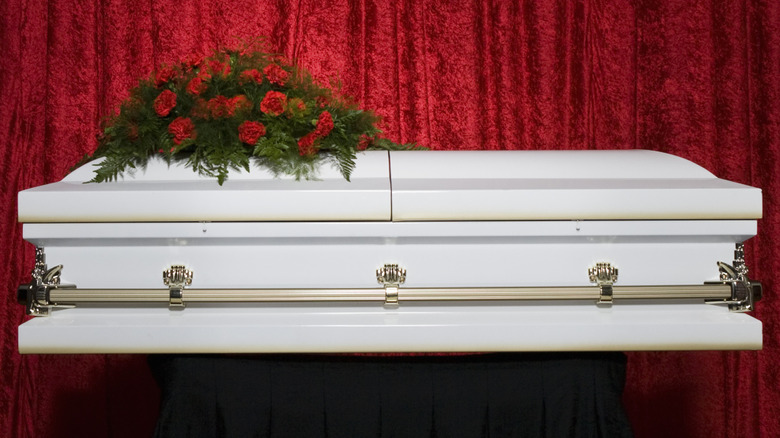 White coffin with red flowers with a red velour curtain behind it