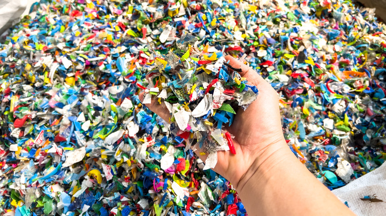 Hand grabs handful of plastic pellets from a large debris bin