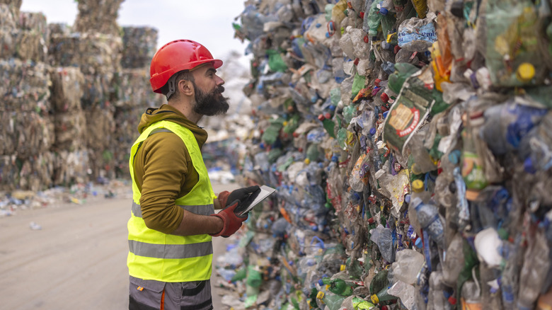 Waste depot employee looks at large mass of plastic waste