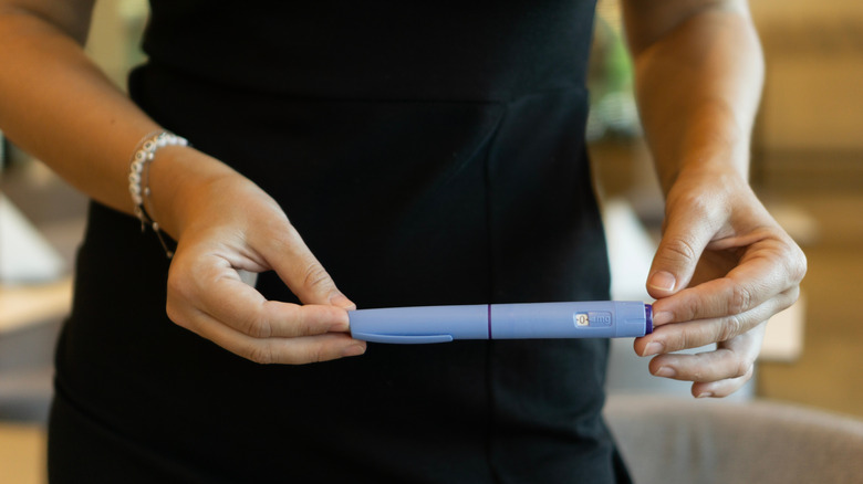 A woman in a black dress holding an Ozempic pen