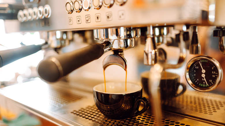 Espresso pouring from an espresso machine into a dark-colored cup. A pressure dial on the machine reads a pressure of about 10 bar.