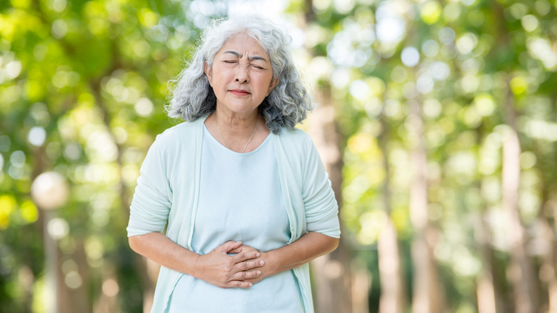 Elderly woman in park grasping belly with pained look on face