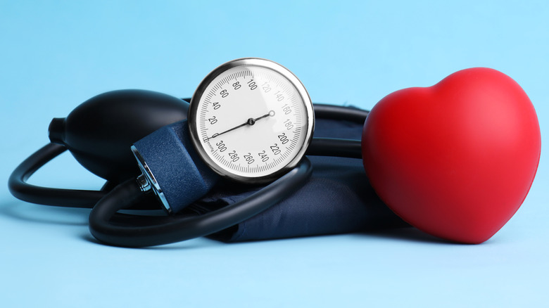 A blood pressure cuff with a red toy heart sitting next to it