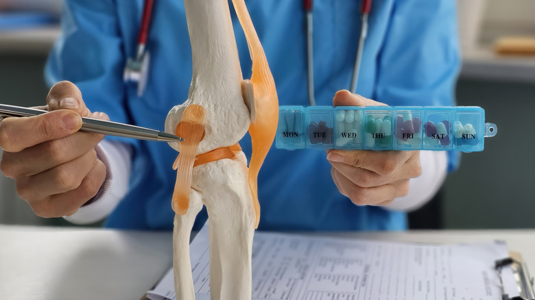 Doctor holding up medicines while pointing to model of knee