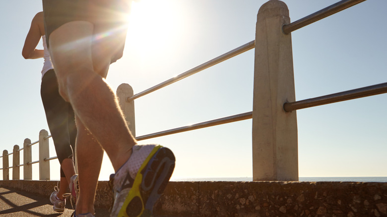 Legs of people running outside with sun in the background.
