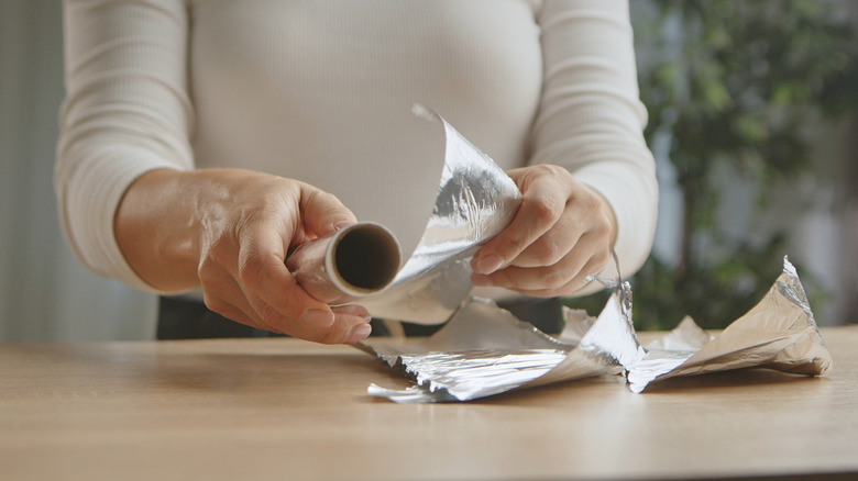 Person unrolling aluminum foil and tearing off pieces