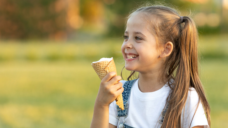 Young white girl eating ice cream cone, smiling in green field