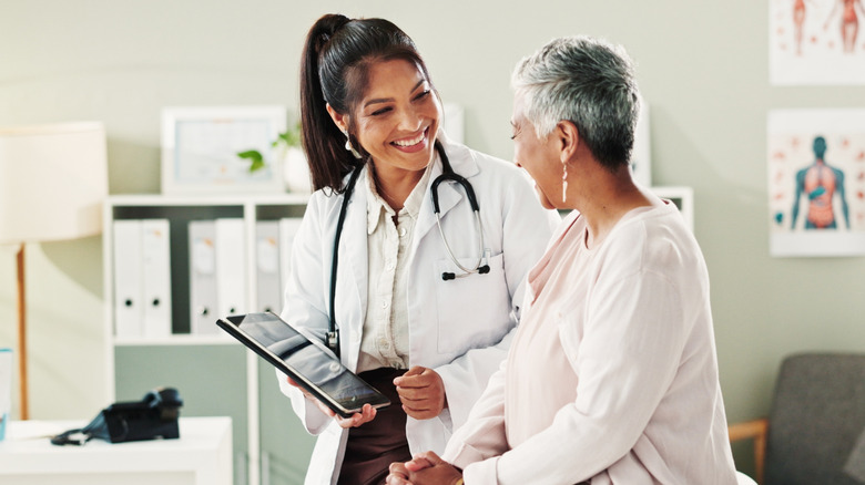 female doctor smiles and shows tablet screen to short haired middle aged woman