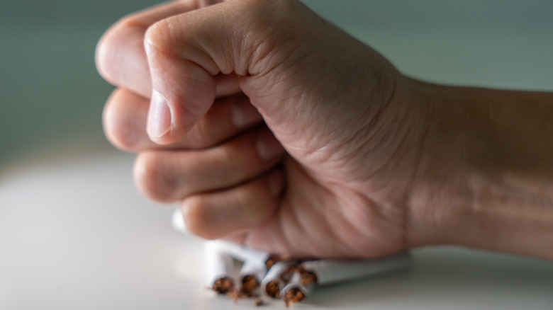 Close-up of a person's fist crushing cigarettes on table