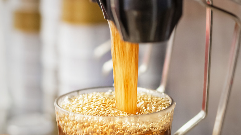 A glass being filled with bubbly, dark brown soda at a soda dispenser.
