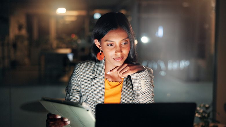 Woman in checked jacket and golden blouse working with a laptop and tablet at night