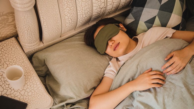 A woman lays in bed wearing an eye mask