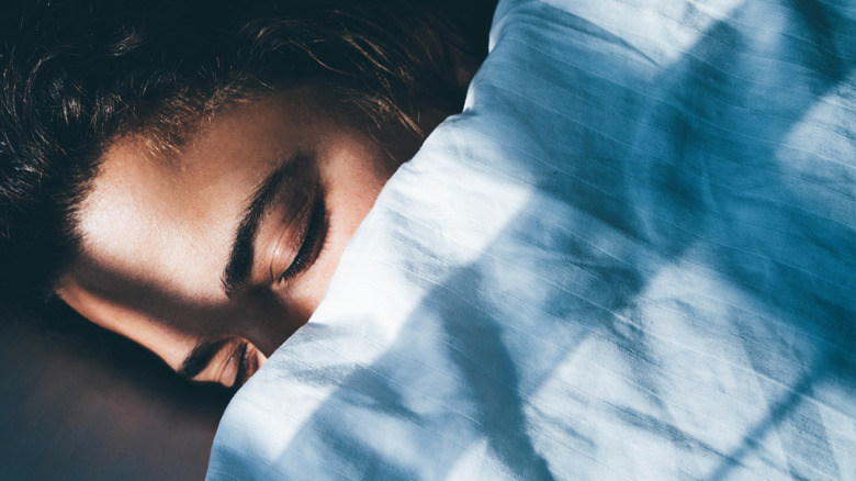 A woman's closed eyes are visible as she lays in bed beneath a blanket