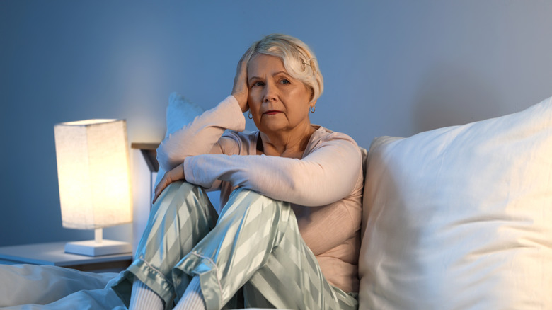 Older woman sitting in bed in pajamas, look of concern on her face
