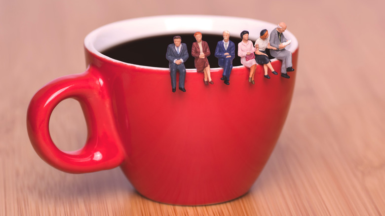 Miniature human figures sitting on the rim of a coffee mug