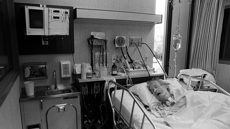 Very sick man in hospital bed who is hooked up to a ventilator and IV drip